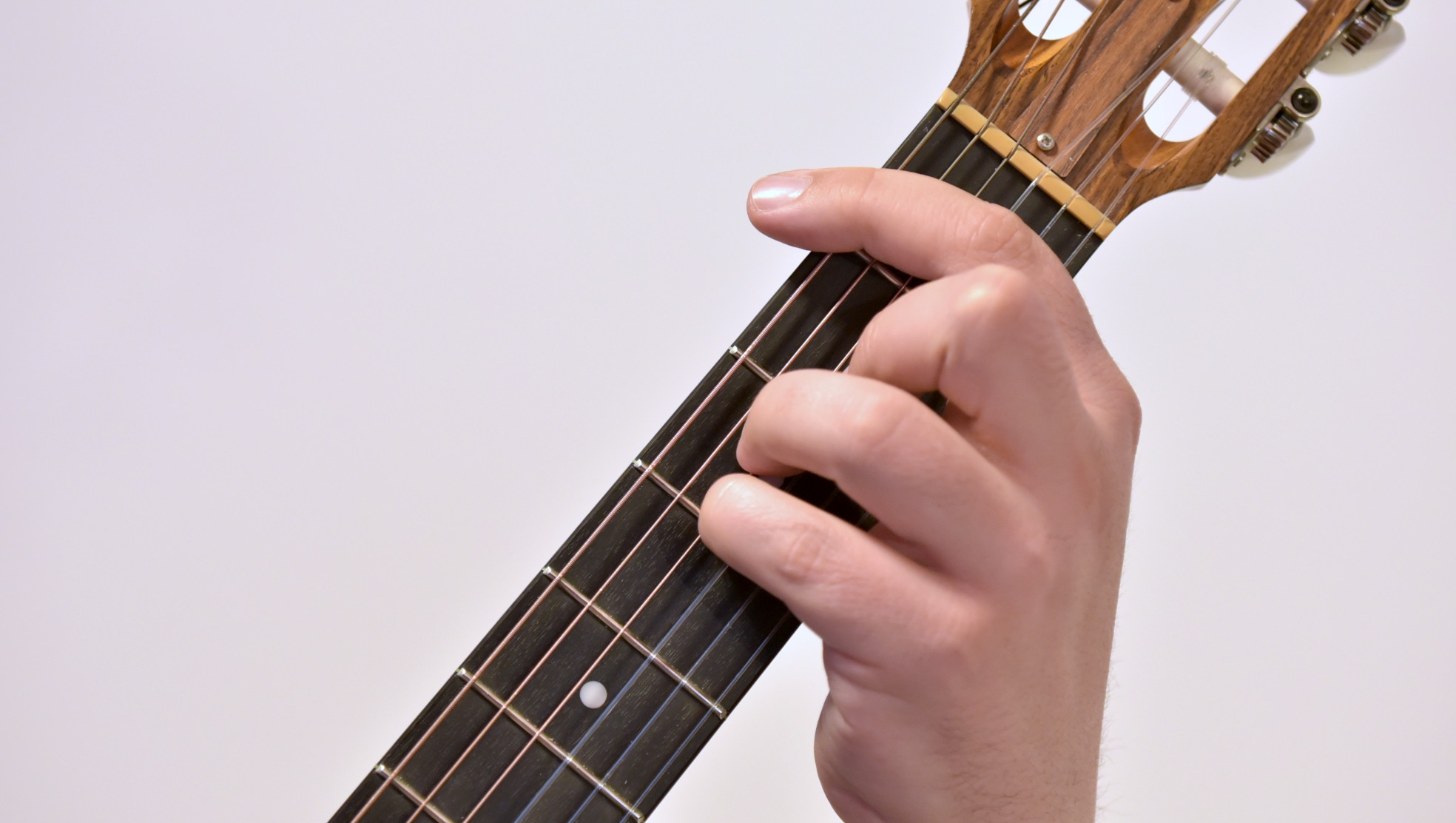 Mano izquierda haciendo cejilla completa en el diapasón de una guitarra clásica